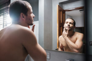 man applying skin care products for men to his face in the mirror