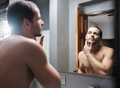 man applying skin care products for men to his face in the mirror